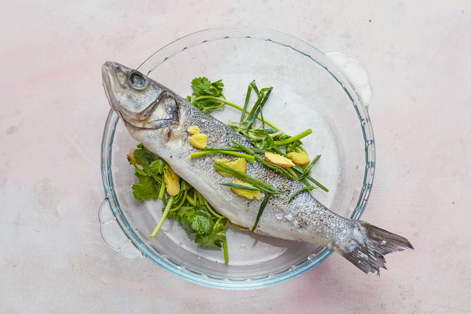 Whole steamed fish with ginger and scallions in a glass bowl.