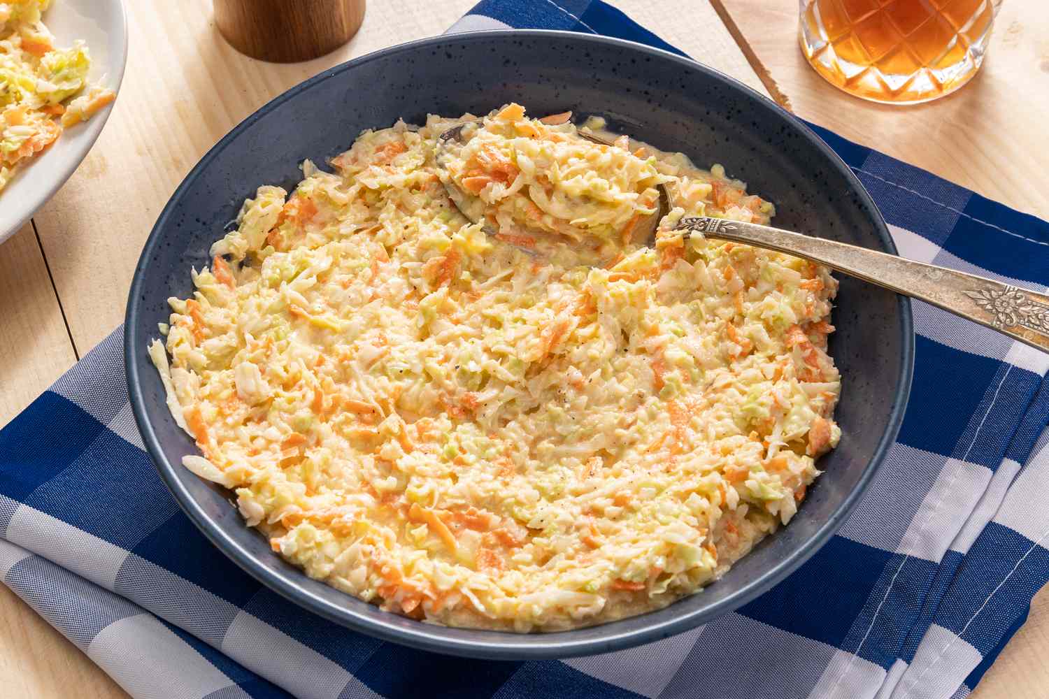 copycat KFC coleslaw in a bowl at a table setting with a glass of iced tea, a pepper grinder, and a plaid table napkin