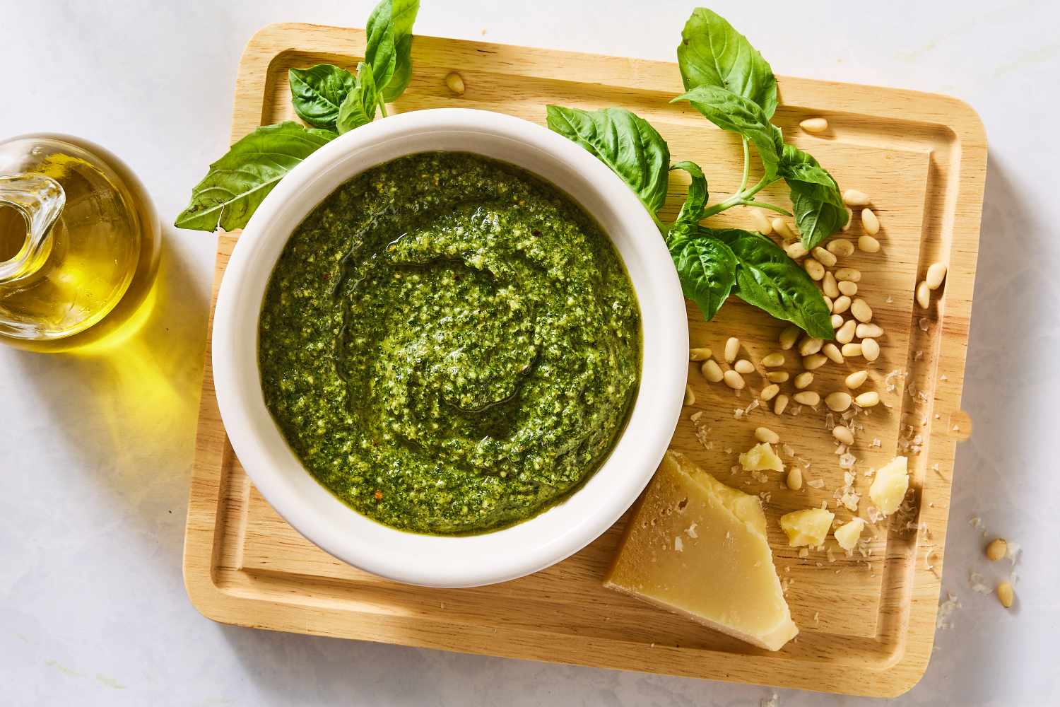 Bowl of basil pesto with basil leaves parmesan cheese pine nuts and olive oil arranged on a wooden board