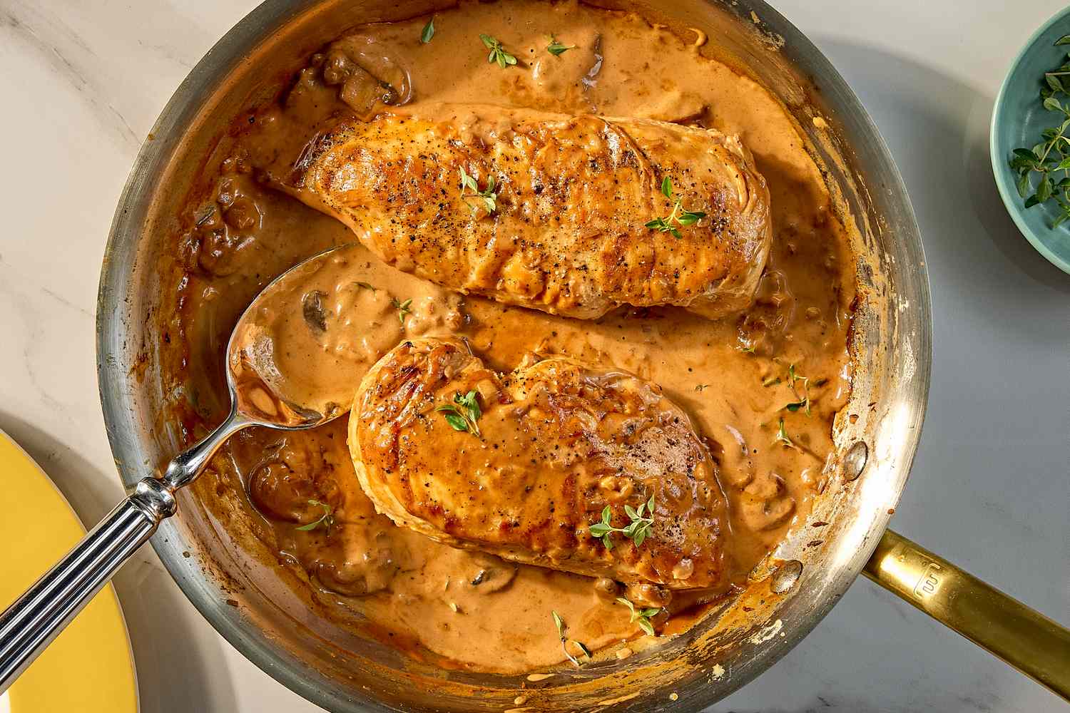 Two cooked chicken breasts in a creamy sauce in a skillet garnished with herbs
