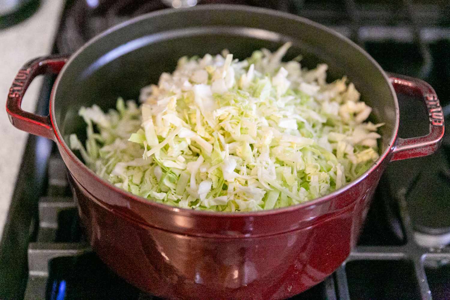 Shredded cabbage placed in a red pot on a stove