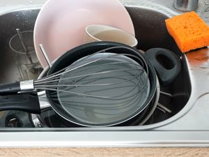 Sink containing dishes pans and cooking utensils with an orange sponge beside it