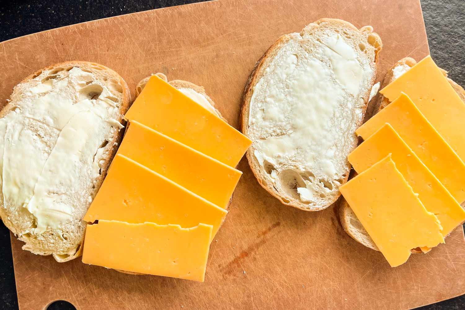 Slices of bread with cheese and butter prepared for making grilled cheese on a cutting board