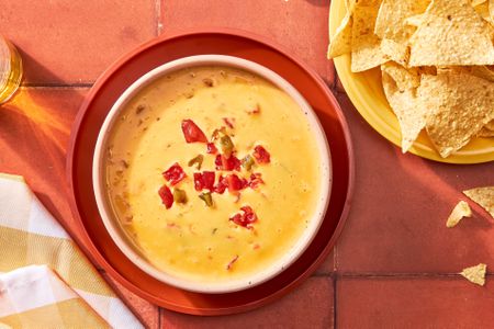 Ro-Tel dip in a bowl at a table setting with a bowl of chips and a glass of beer