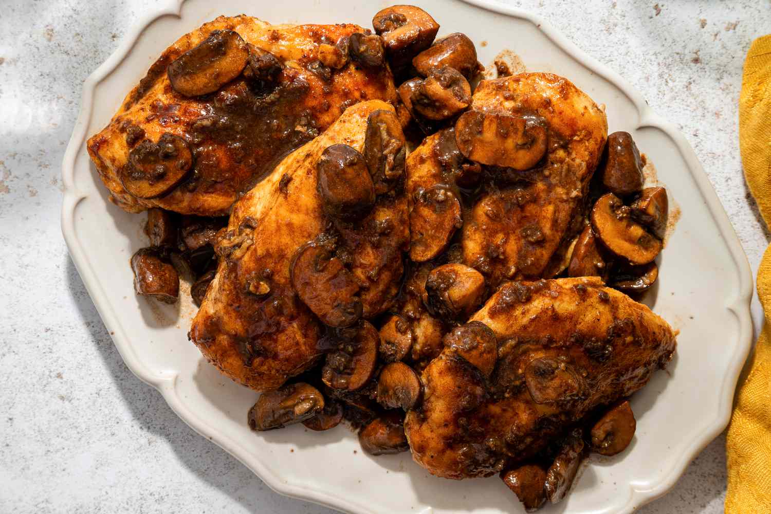 Four chicken breasts with balsamic mushrooms on a white serving plate