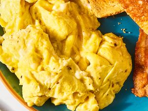 Plate with scrambled eggs toast and a piece of bacon