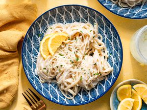 creamy lemon riccotta pasta in a bowl surrounded by a table napkin, a glass of water, and a bowl of sliced lemons