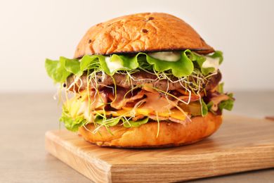 A gourmet burger with lettuce, sprouts, cheese, and mayo on a wooden surface