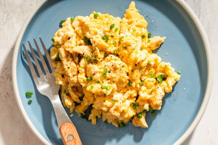 A plate of scrambled eggs garnished with herbs served with a fork