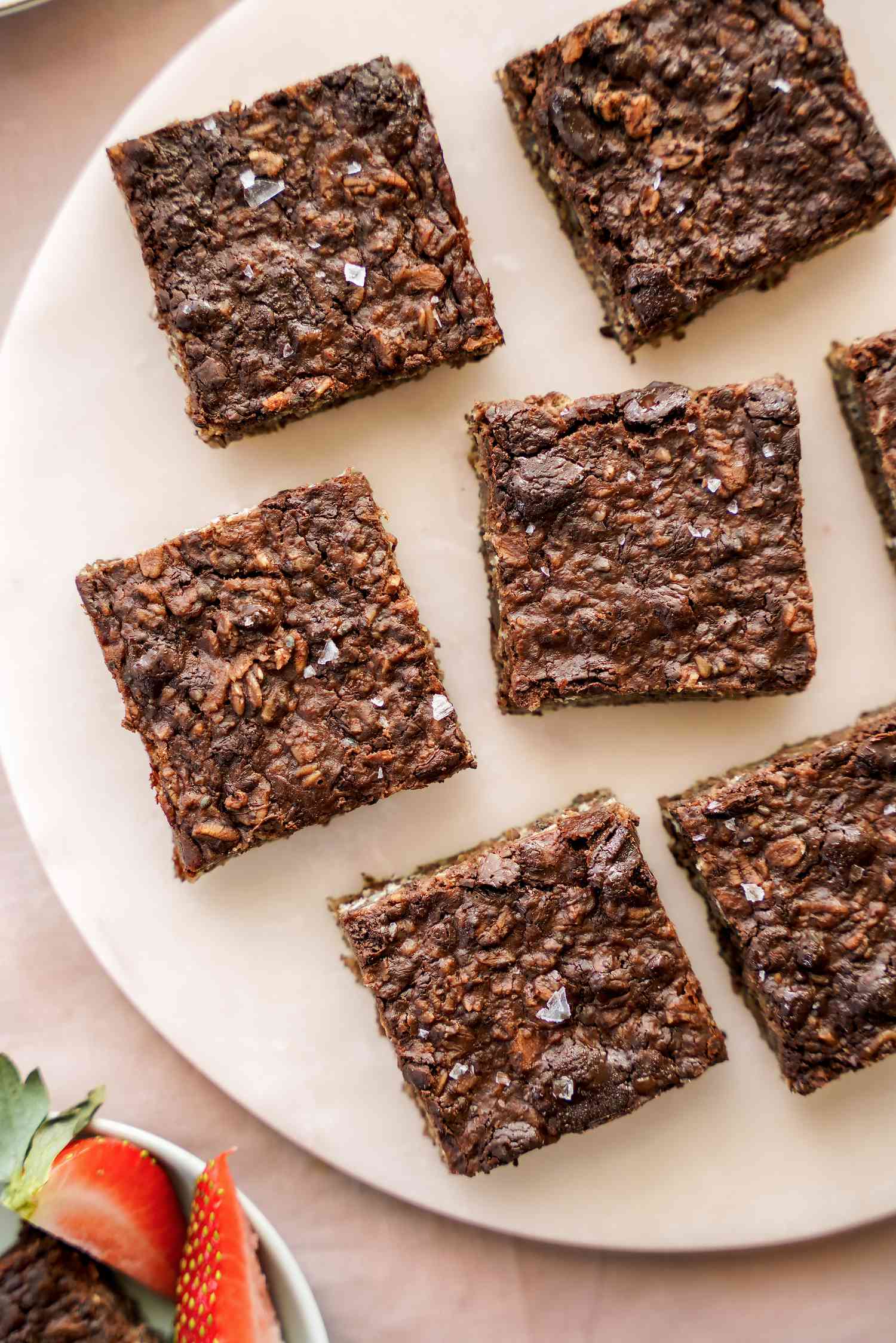 Vegan Brownie Baked Oatmeal on a Plate Next to a Bowl with a Brownie and Quartered Strawberries