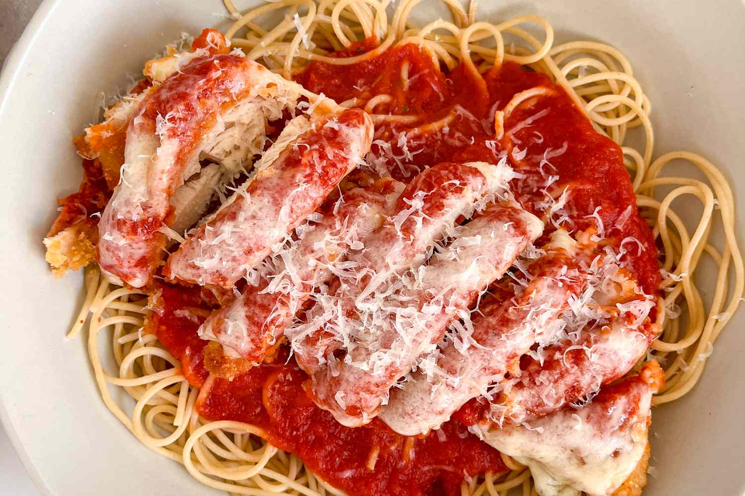 Bowl of chicke parmesan served over pasta with tomato sauce
