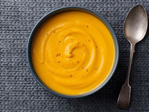A bowl of butternut squash soup with a spoon on a textured surface