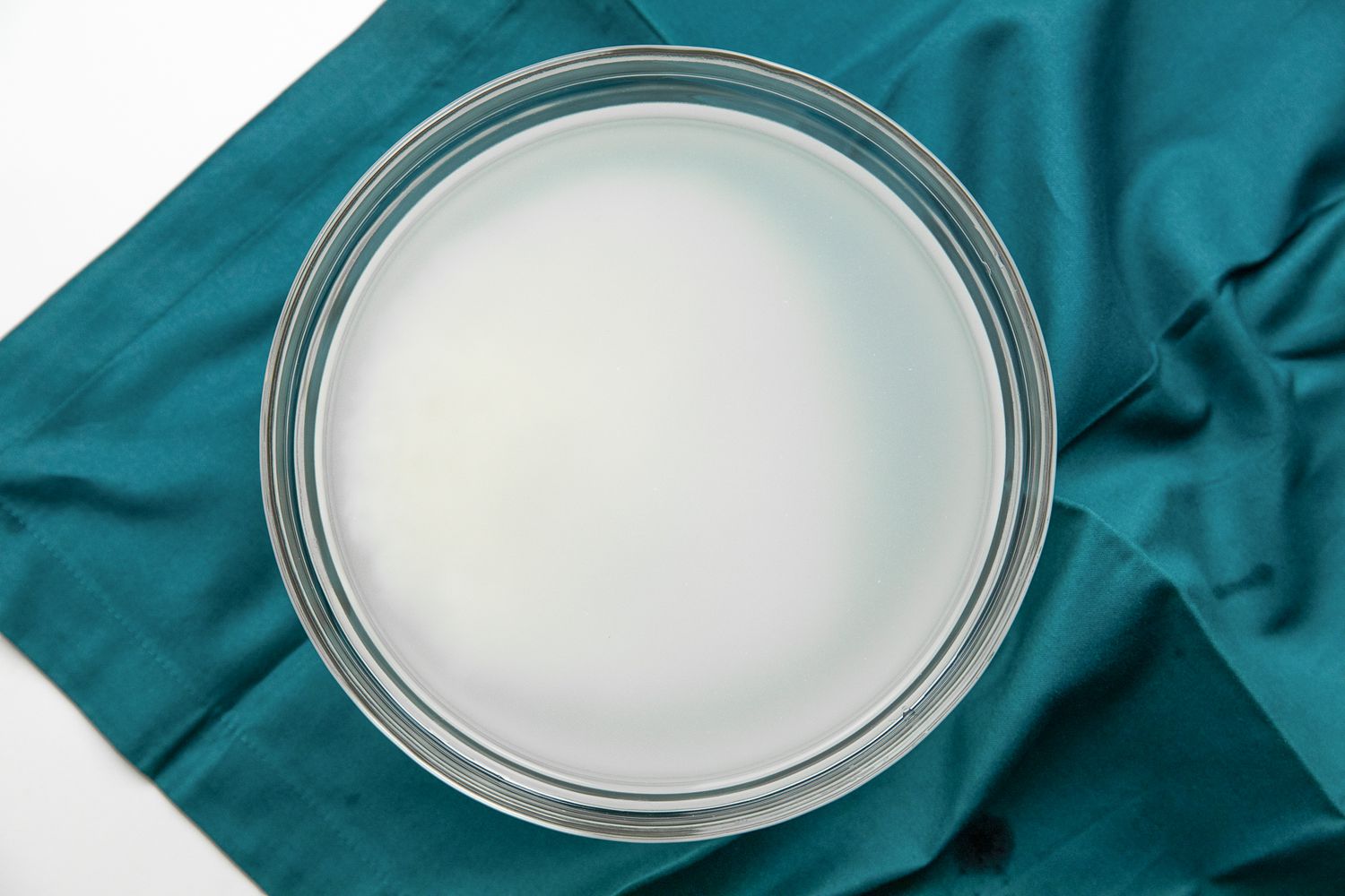 Washing Rice: Rice in a Bowl of Murky Water on a Teal Kitchen Linen for Chicken Congee Recipe