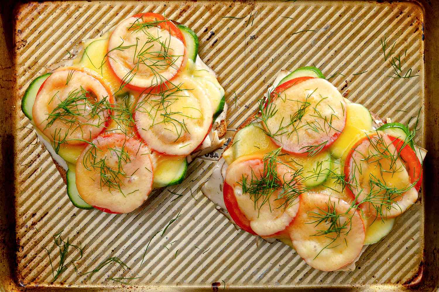 Openfaced sandwiches topped with sliced vegetables and dill on a baking tray