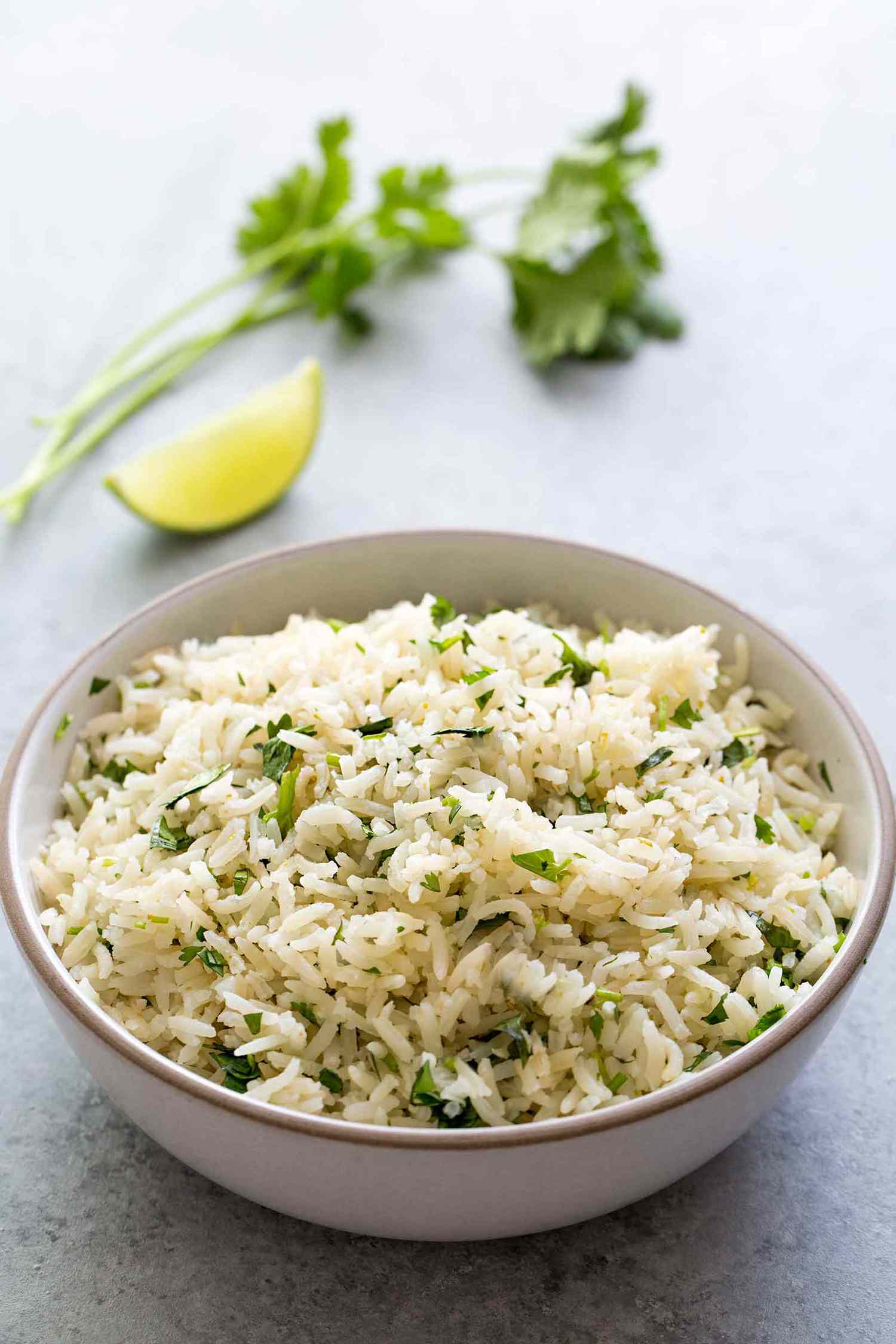 A bowl of cilantro lime rice with a cilantro and a lime wedge in the background