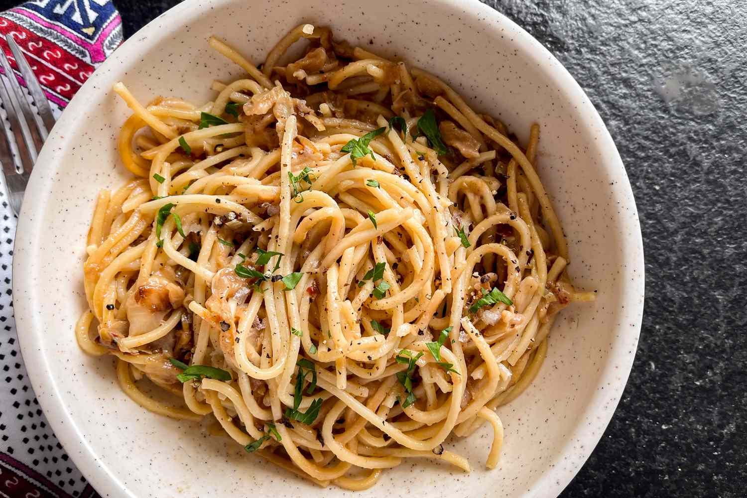 A white bowl with caramelized cabbage spaghetti, garnished with chopped parsley
