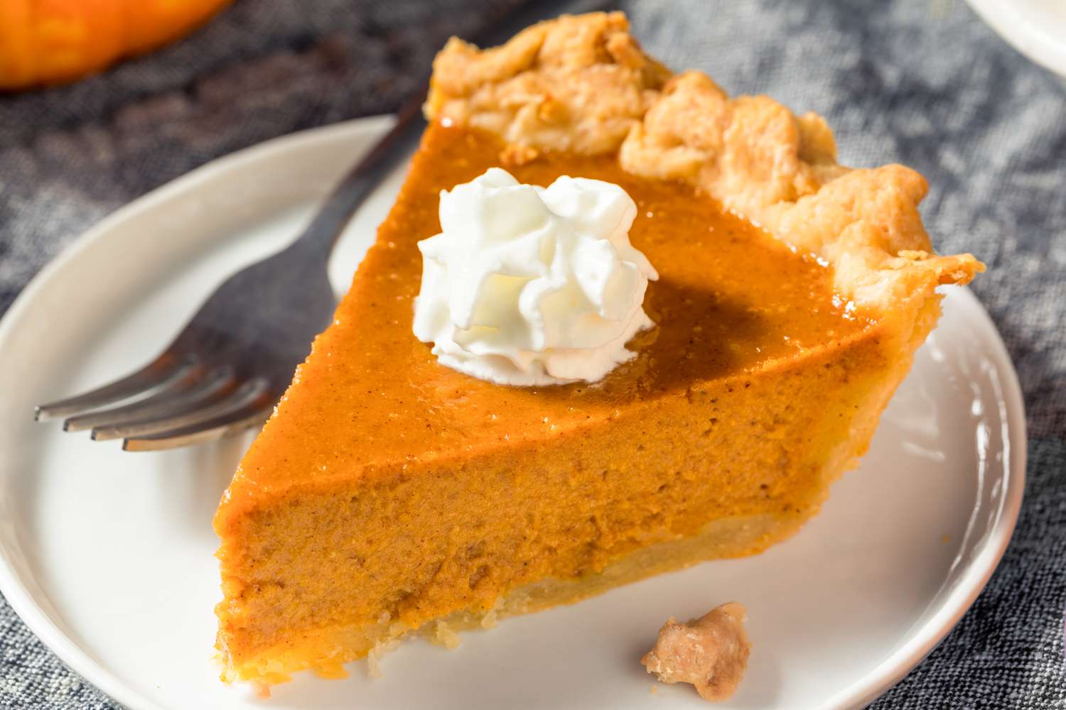 A slice of pumpkin pie with a dollop of whipped cream on top, on a small plate with a fork