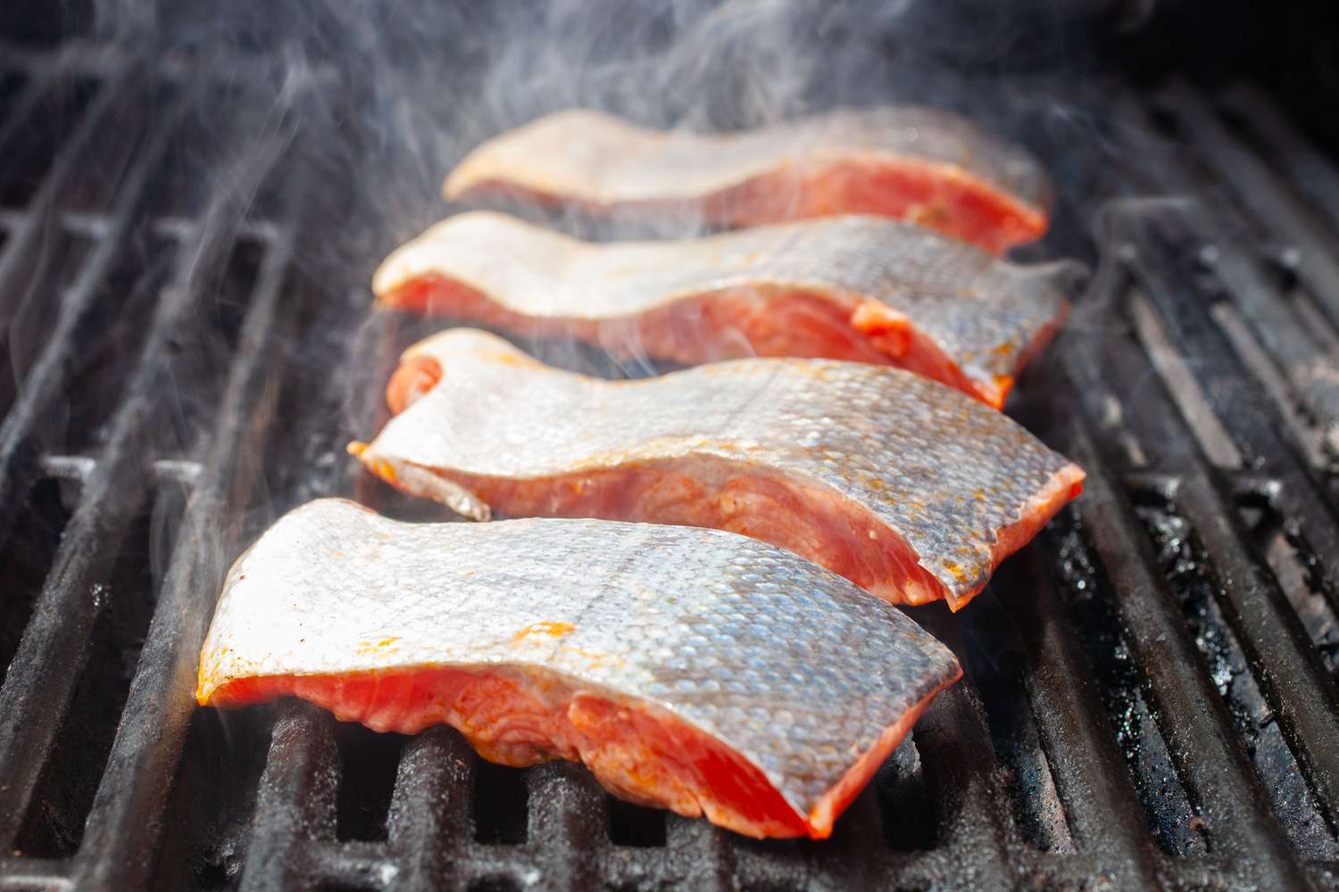 Four salmon fillets being grilled skin-side up