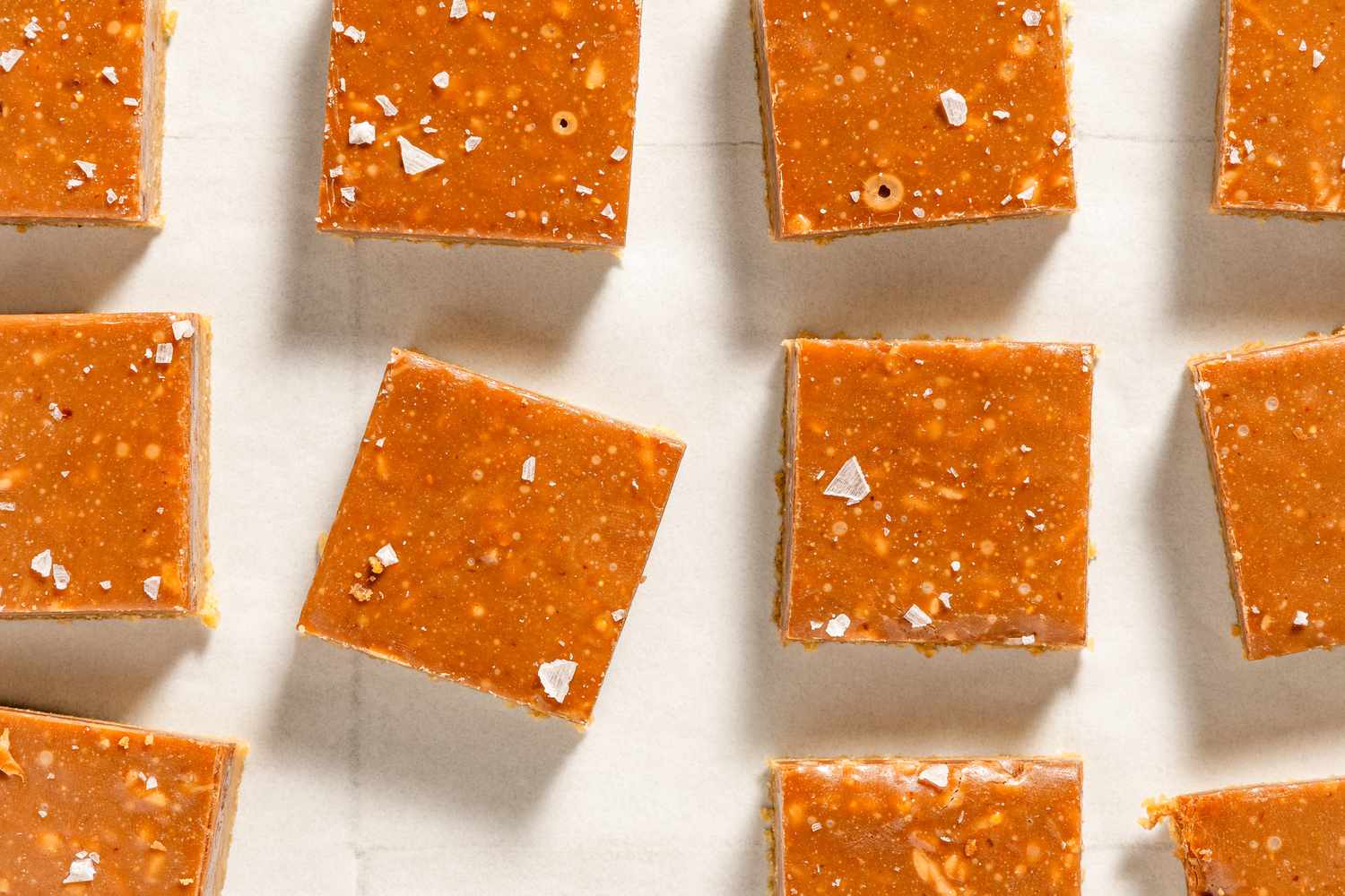 Small caramel squares sprinkled with salt arranged neatly on a parchment paper surface