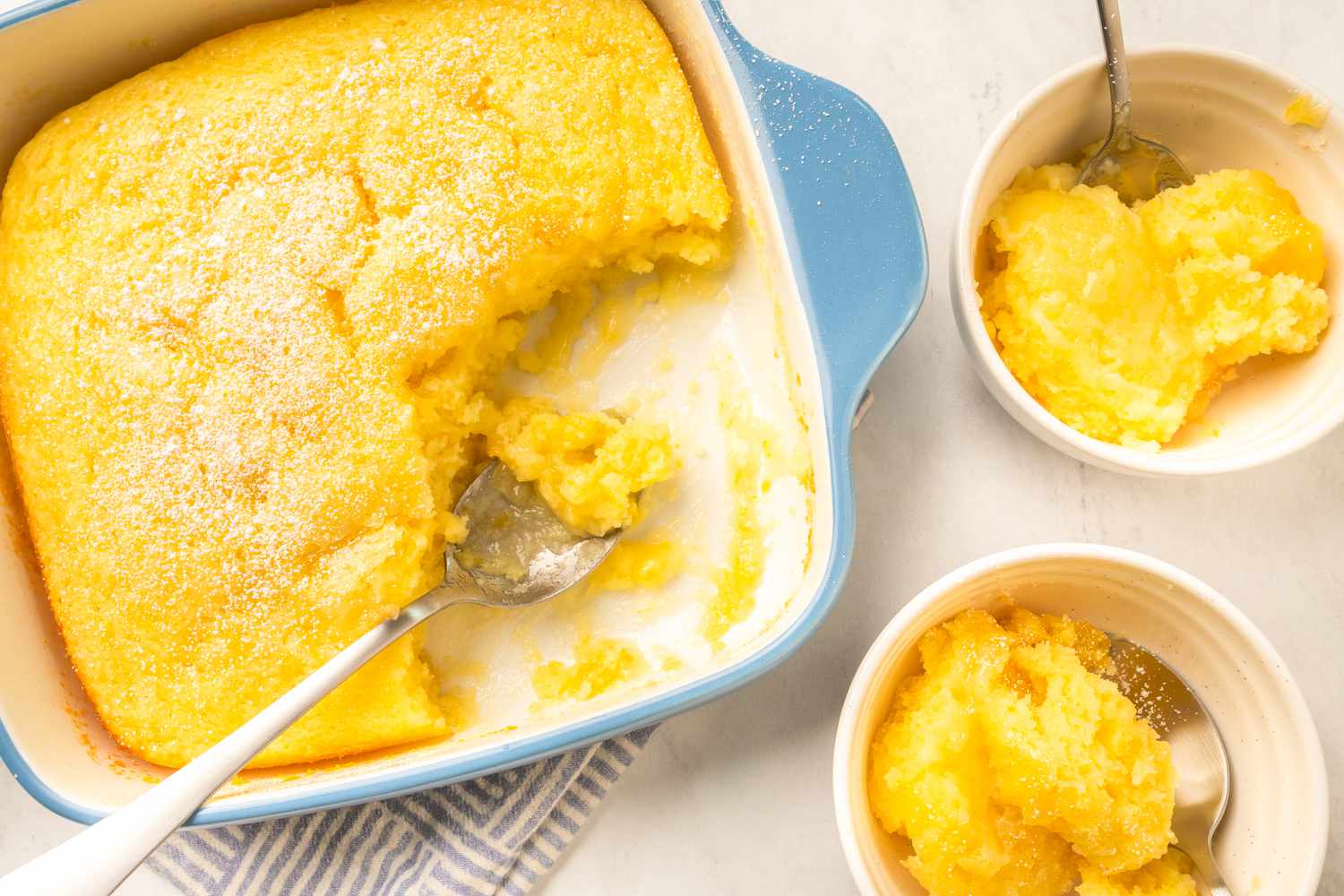 Overhead shot of a baking dish with lemon pudding cake next to two bowls with a serving of the cake