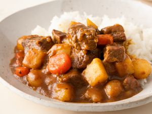 A serving of Korean curry rice with chunks of meat, potatoes, carrots, and curry sauce next to steamed rice