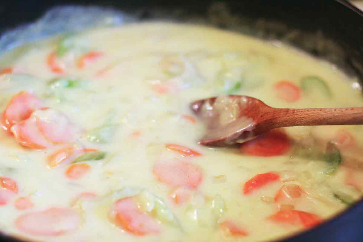 Homemade chciken pot pie filling thickening in a skillet and stirred with a wooden spoon.
