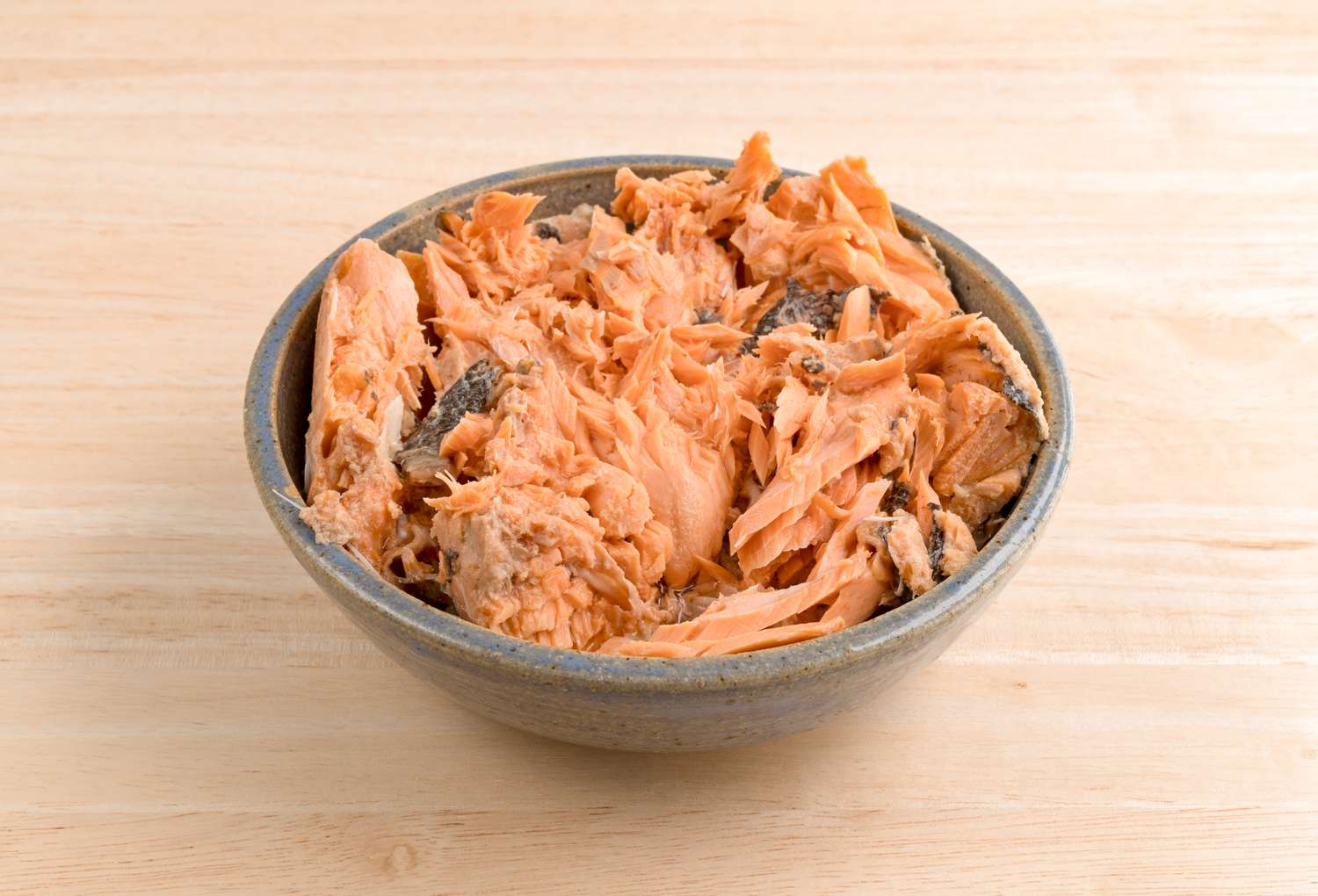 Canned salmon in a bowl on a wooden counter