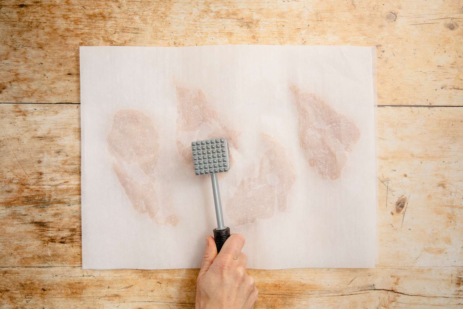 chicken flattened between two pieces of parchment using a meat tenderizer for chicken marsala recipe
