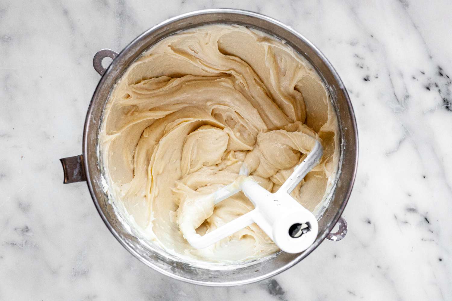 The bowl of a stand mixer with frosting inside to make the best carrot cake recipe.
