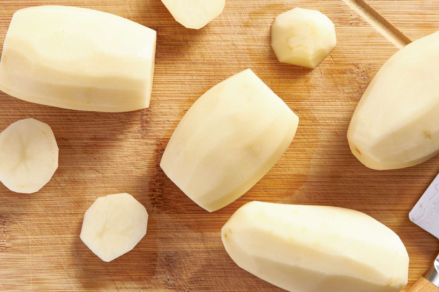 Peeled russet potatoes on a cutting board for fondant potatoes recipe