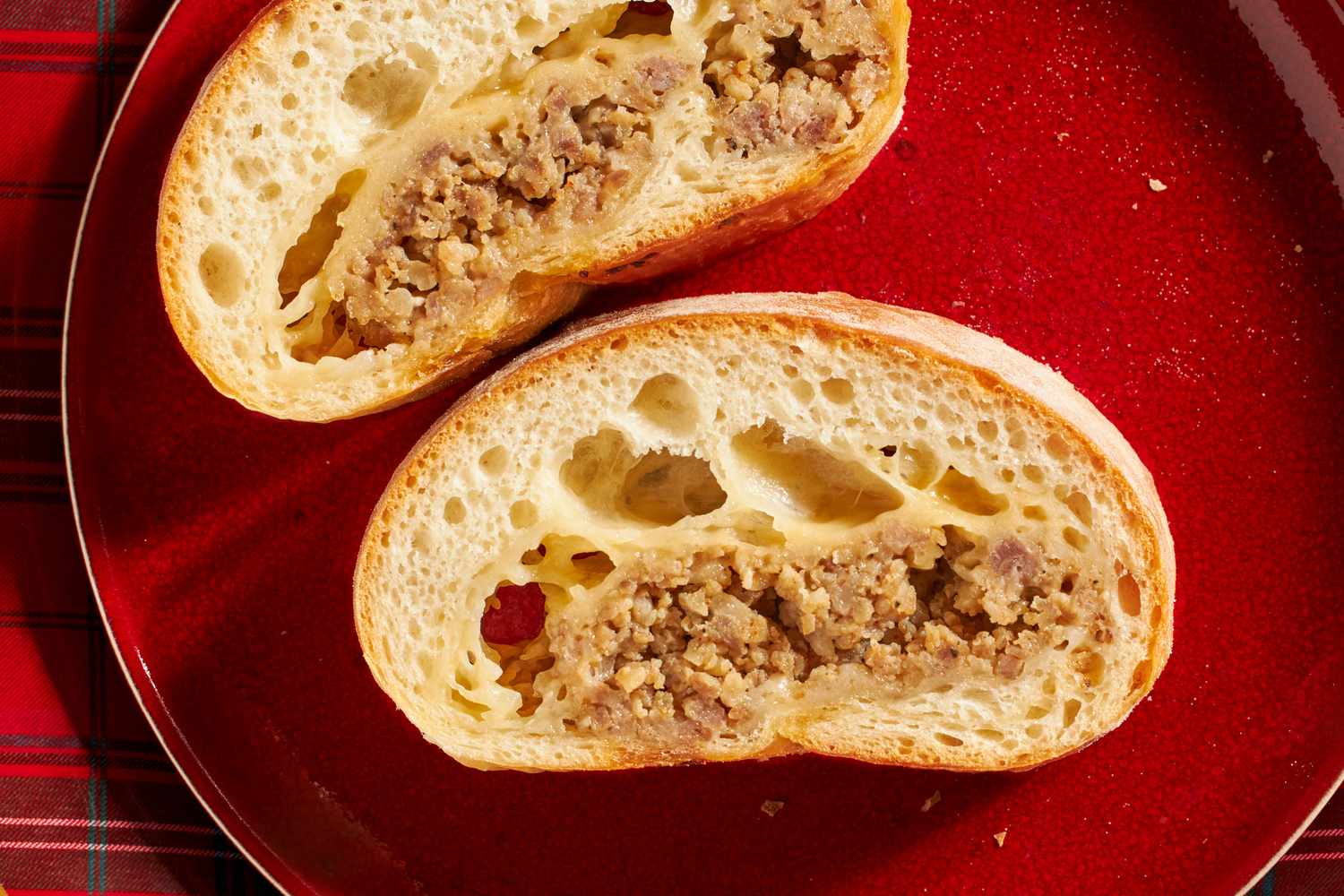 Two slices of bread packed with cooked sausage filling served on a red plate