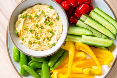 Bowl of curry dip surrounded by fresh vegetables including cucumbers, yellow peppers, snap peas, and tomatoes