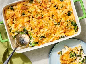Overhead view of chicken and broccoli casserole in a green dish with a serving spoon next to a small plate with a serving