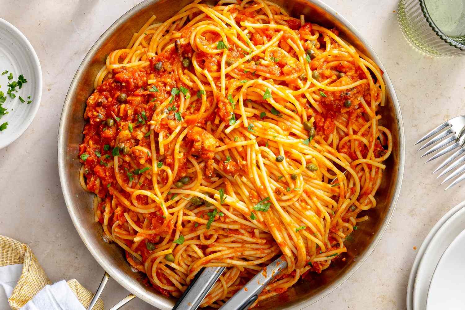 A plate of pasta with a tomatobased sardine sauce and a fork and spoon in the pan