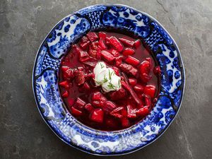 Beet Borscht in a blue bowl with a spoonful of sour cream on top