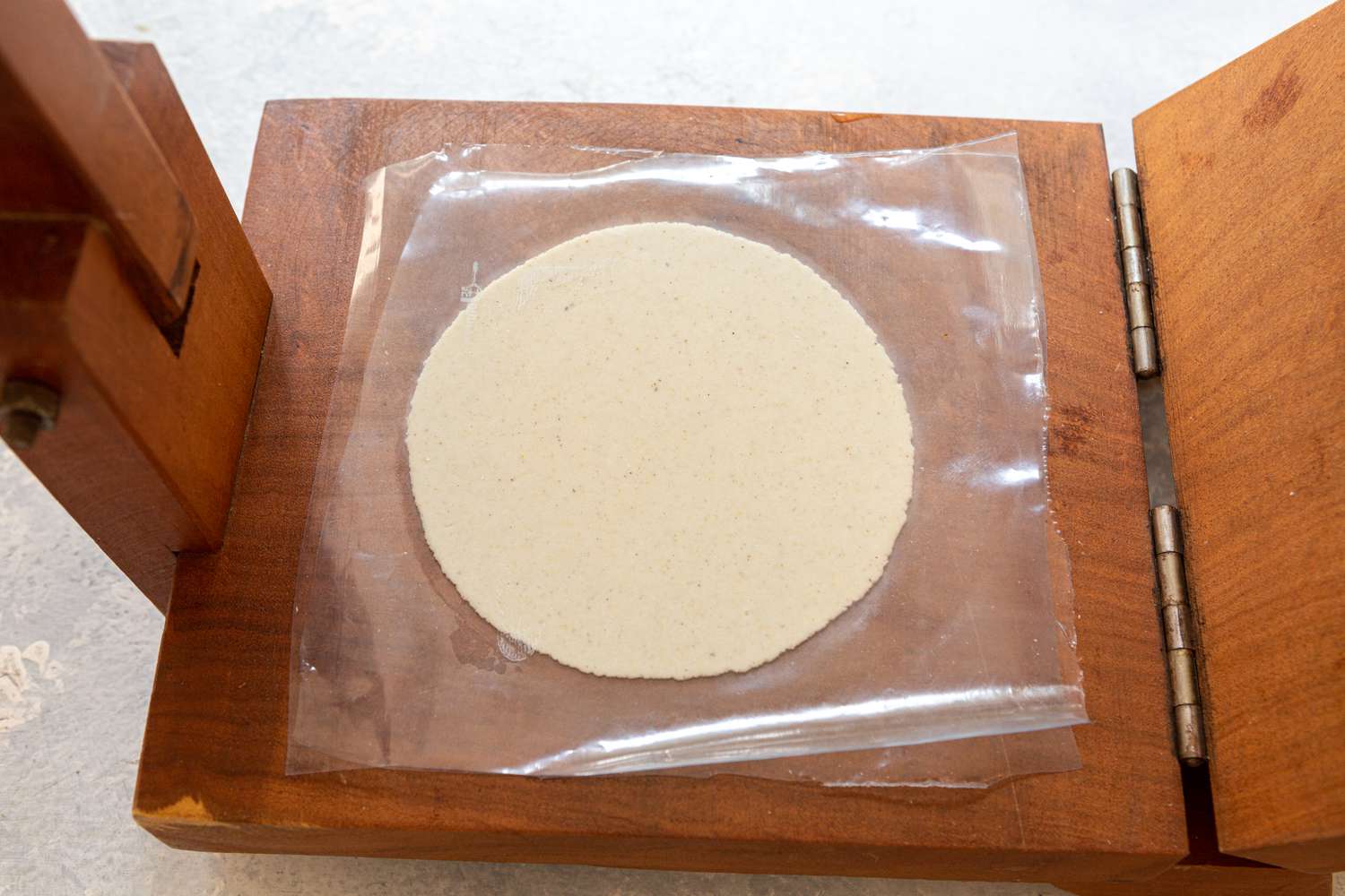 A pressed tortilla in a tortilla press with plastic on top 