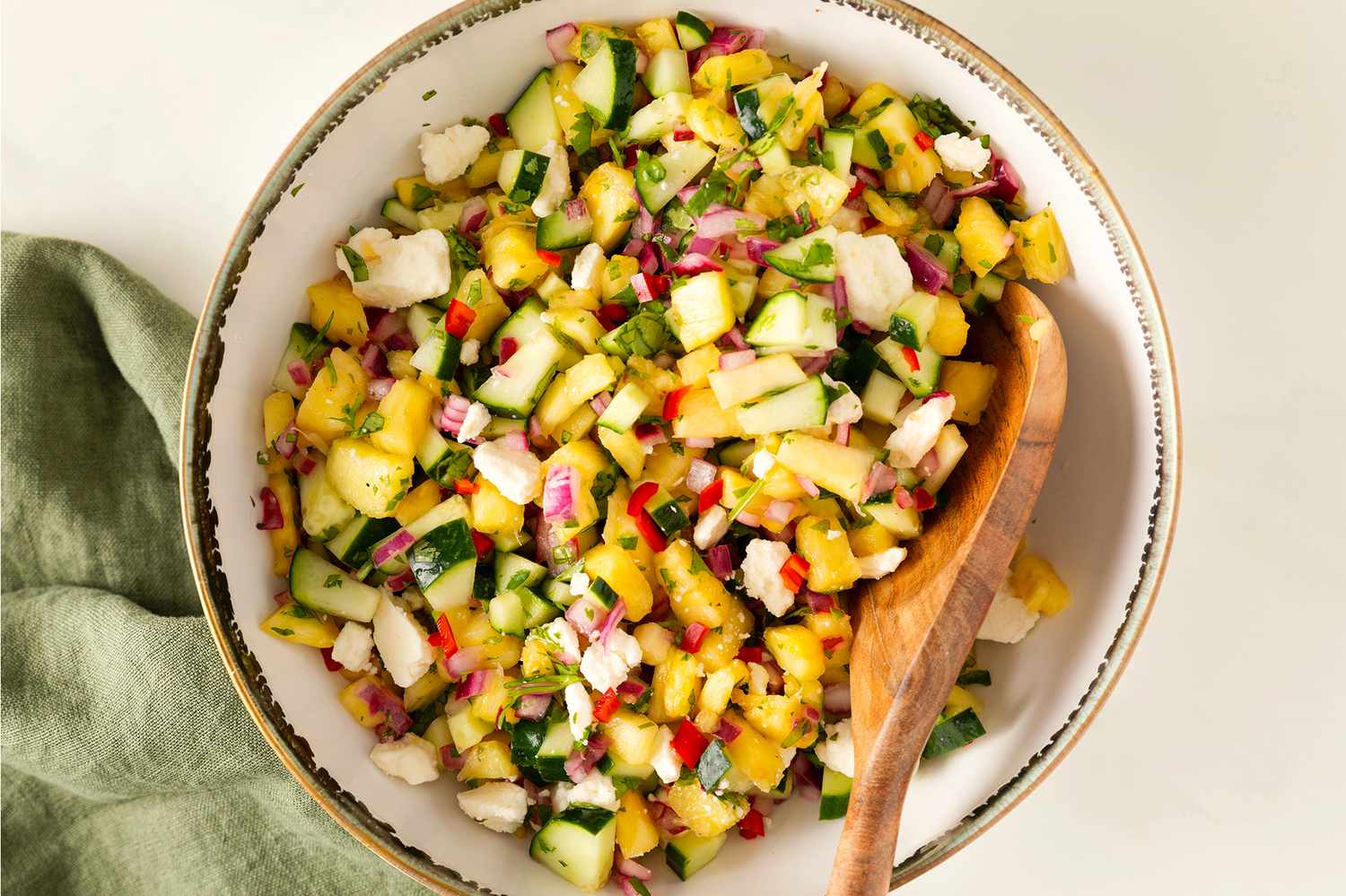 Pineapple Cucumber Salad with Feta in a serving bowl with a wooden spoon