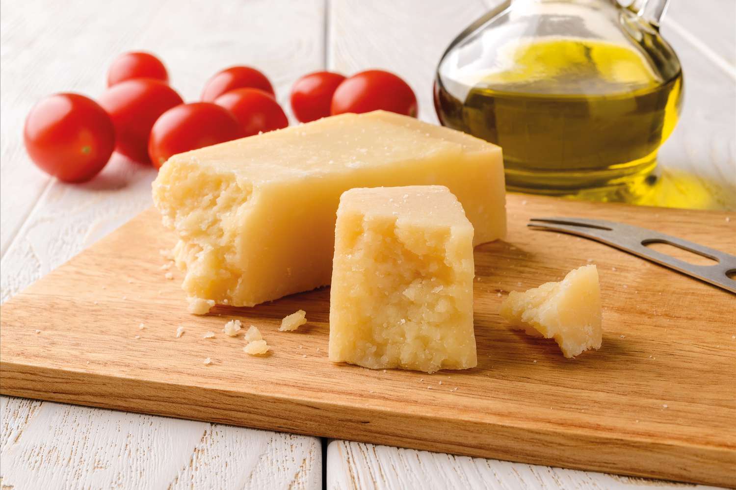 blocks of parmesan on a cutting board and in the background, grape tomatoes and a carafe of olive oil