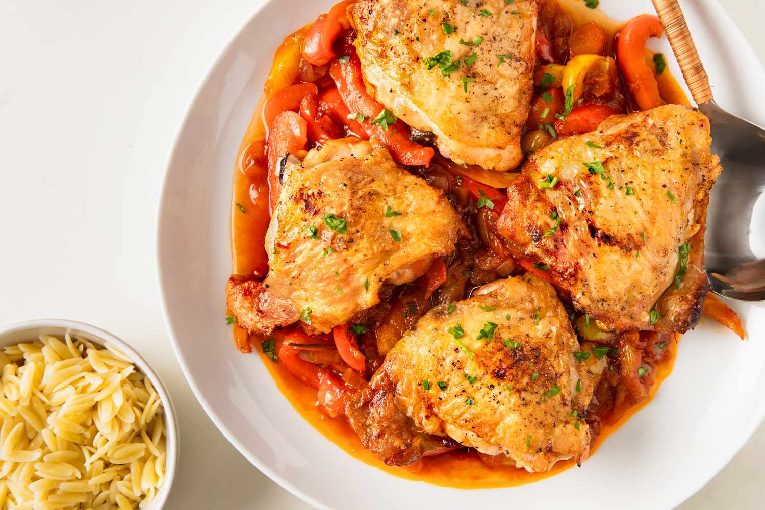 Plate of cooked chicken over a bed of vegetables served alongside a dish of orzo pasta