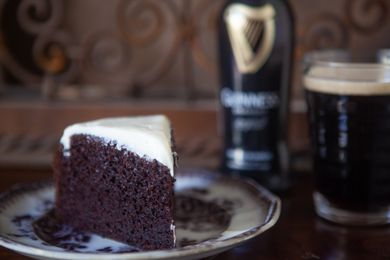 A Slice of Chocolate Guinness Cake on a Plate and in the Background, a Bottle of Guinness and More in a Glass 