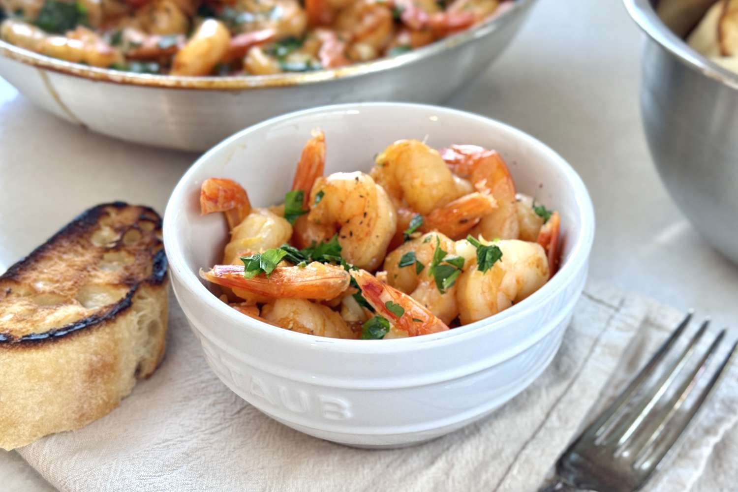 Bowl of garlic shrimp on a table with a slice of toasted bread beside it