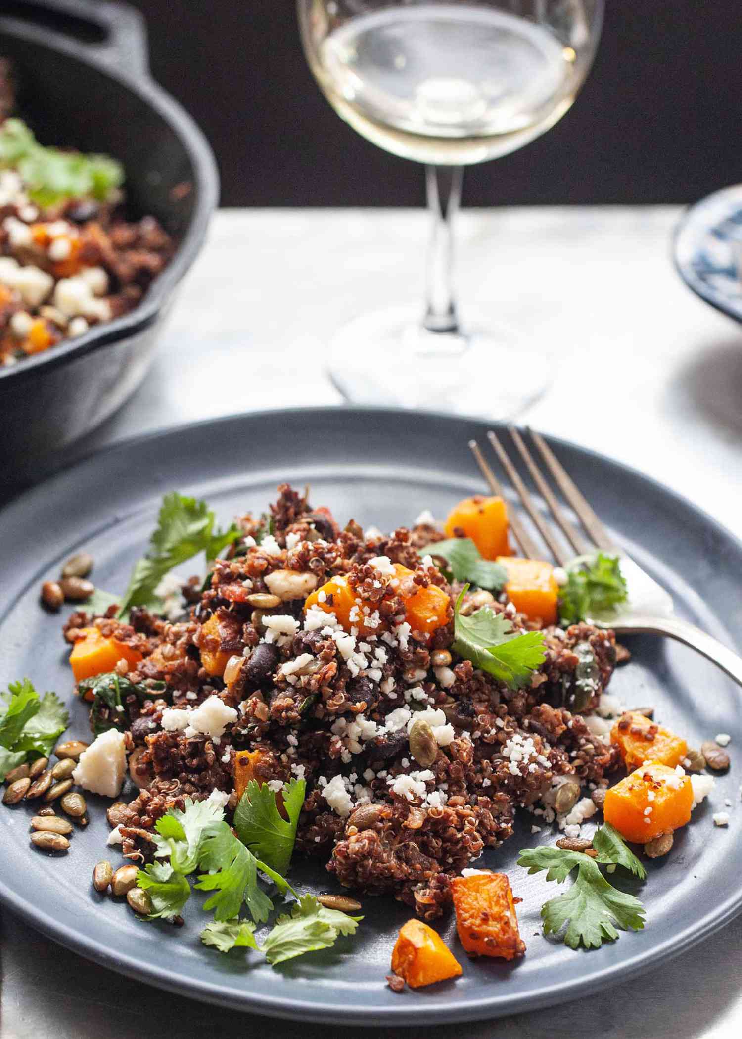 A side view of easy vegetarian skillet dinner on a grey plate with a fork on the upper right. A glass of white wine is above the plate.