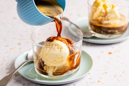 Espresso being poured over ice cream in a glass affogato dessert