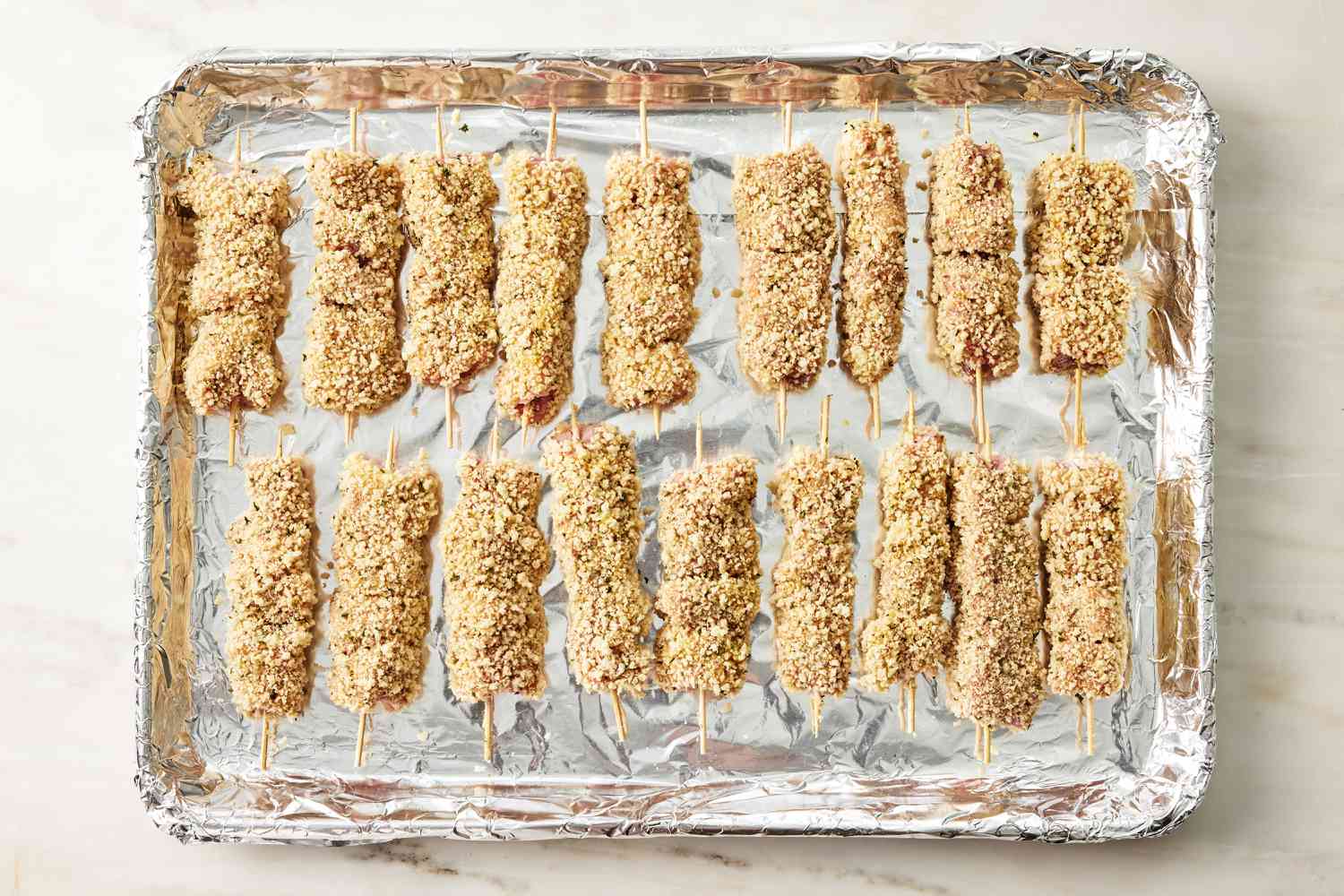 breaded, skewered chicken on a foil lined baking sheet for City Chicken recipe