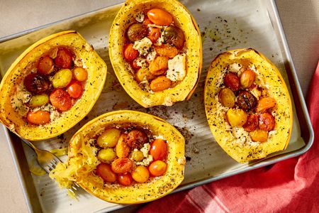 Overhead shot of four baked spaghetti squash stuffed with feta and cherry tomatoes, on a baking sheet