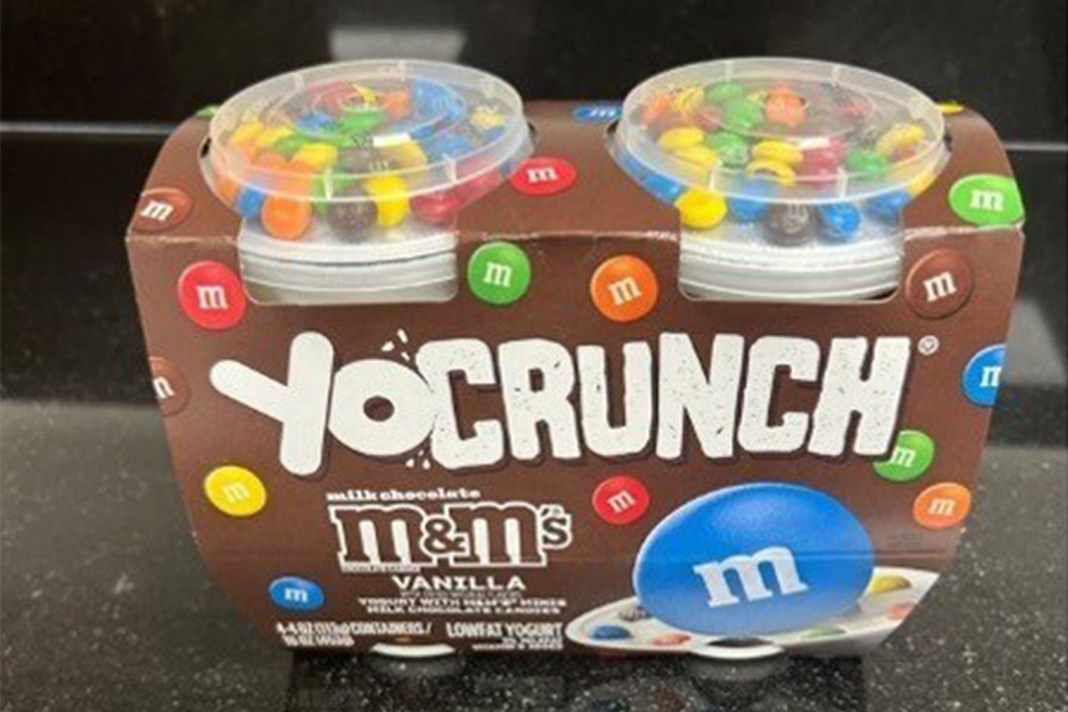 YoCrunch vanilla yogurt with MMs topping shown in packaging on a black surface