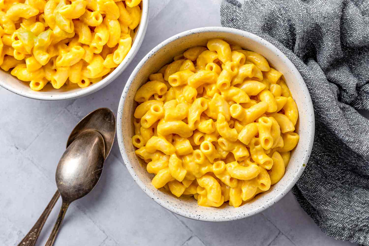 Two Bowl of Vegan Mac and Cheese Next to Two Spoons and a Table Napkin