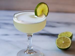A chilled coupe with a frothy gin cocktail to show what a gimlet is.