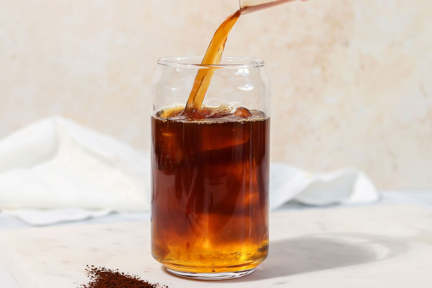 Glass iced coffee being poured with granules in the forground