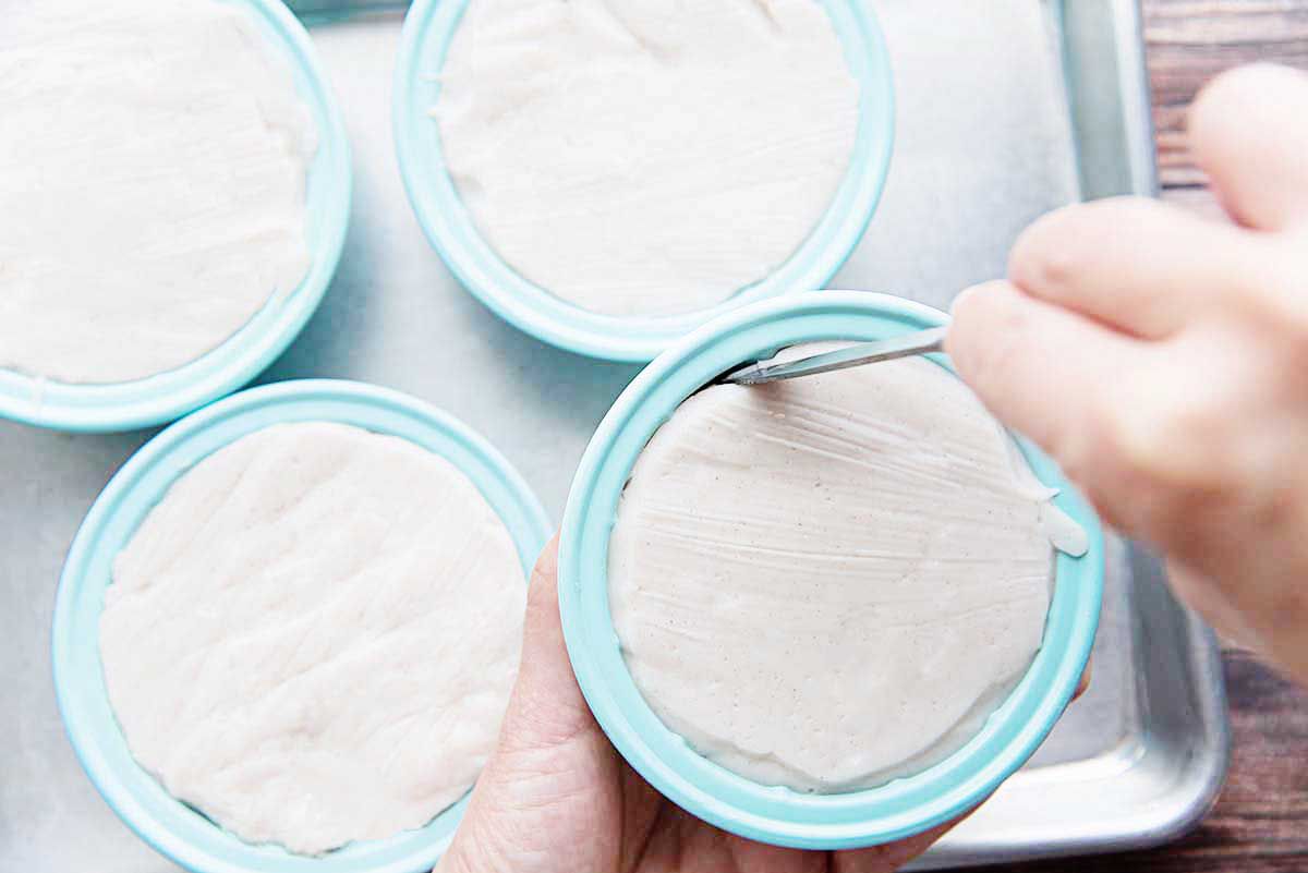 Four teal molds with the best coconut pudding inside. A knife is running around the edge to help unmold the pudding. Three others are on a baking tray.